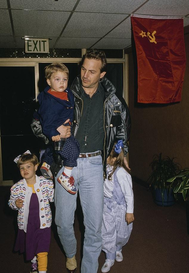 Кевин Костнер несёт на руках сына Джо, а рядом идут его дочери Лили и Энни, 1990 г