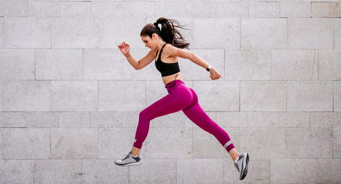 Уверенная и энергичная спортивная молодая женщина, прыгающая в воздухе над серым фоном.