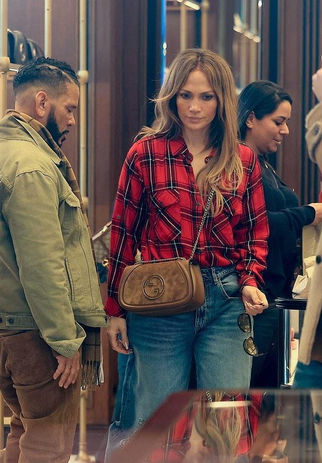 Пока семья рассматривала люксовые товары в магазине Gucci, Дженнифер стянула свое тяжелое пальто, чтобы остыть, открыв свою коричневую замшевую сумку и клетчатую рубашку.